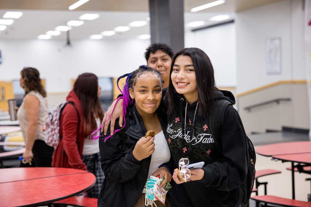 Two high school students smile at the camera during lunch time.