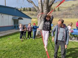 child walks on outdoor tight rope while adult and other kids look on
